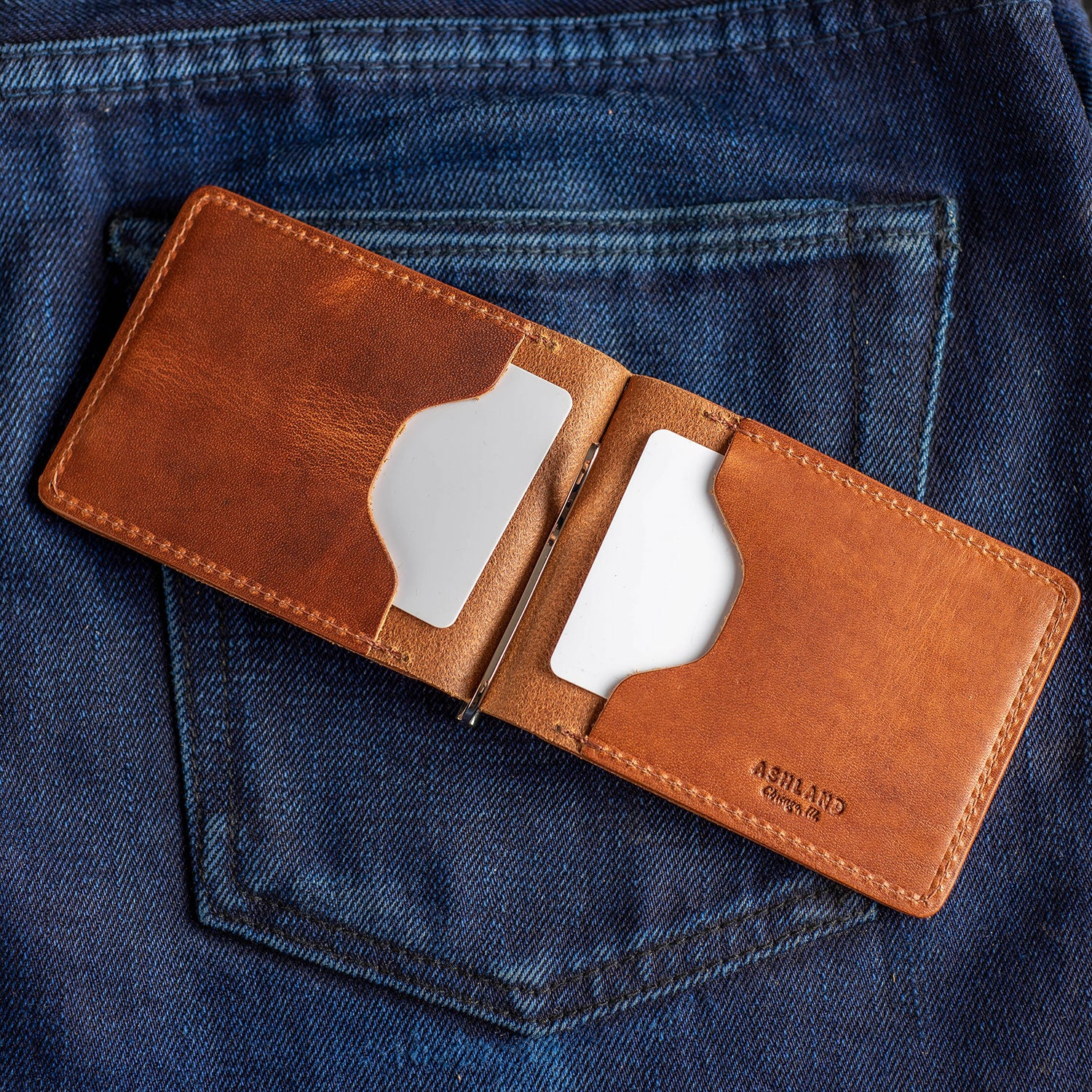Capone Money Clip folded open revealing two card pockets and the metal clip fastener, sitting on blue selvedge jeans