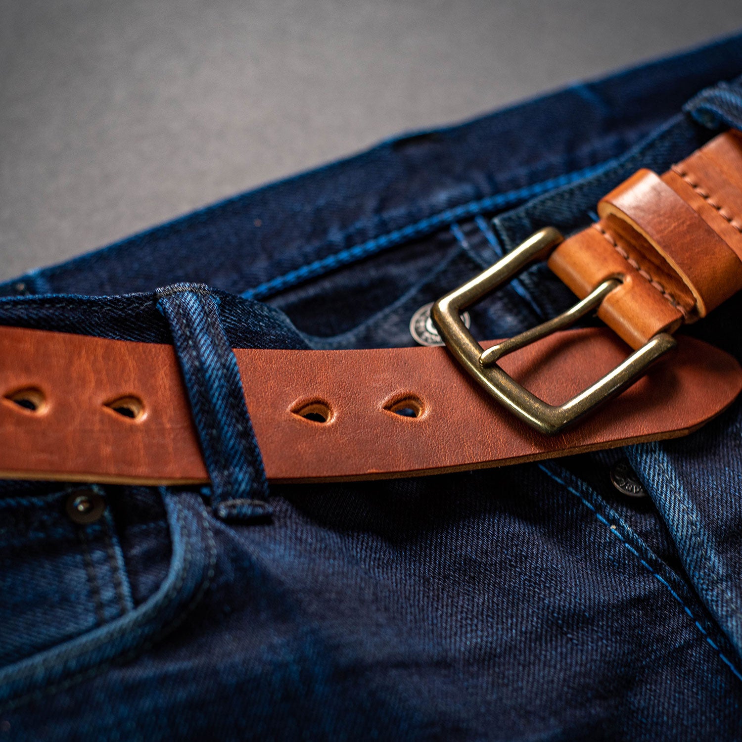 leather belt for men, horween leather, shown laying flat on men's selvedge jeans